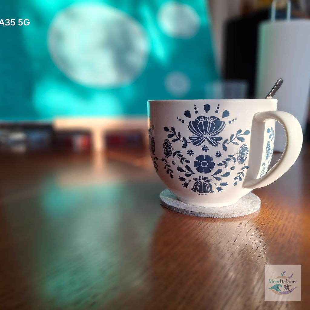 Weiße Tasse mit blauem Blumenmuster auf einem Tisch vor unscharfem Hintergrund