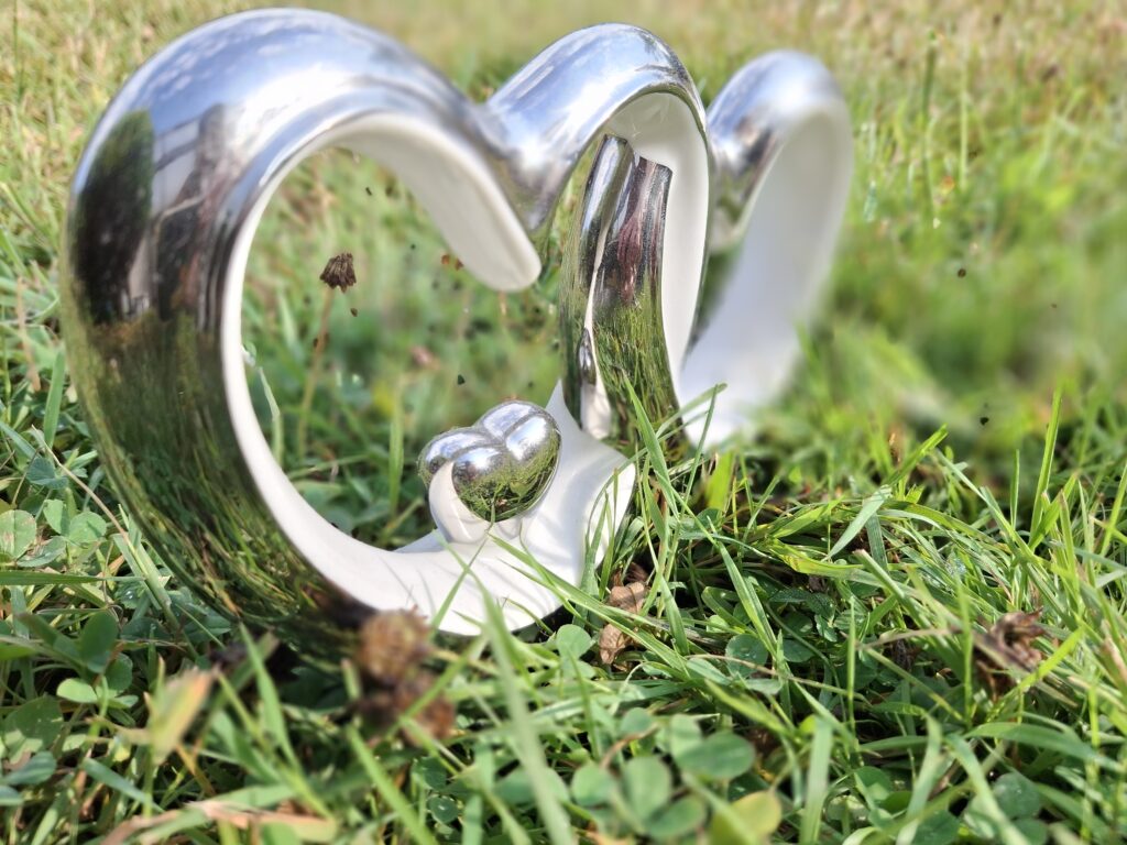 Silberglänzende Herzskulptur aus zwei ineinandergreifenden Herzen im grünen Gras.