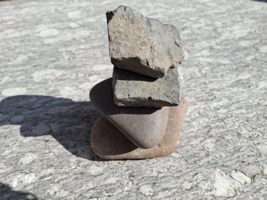 Drei sorgfältig übereinandergestapelte Steine auf einem Felsen vor einem ruhig verschwommenen Naturhintergrund.