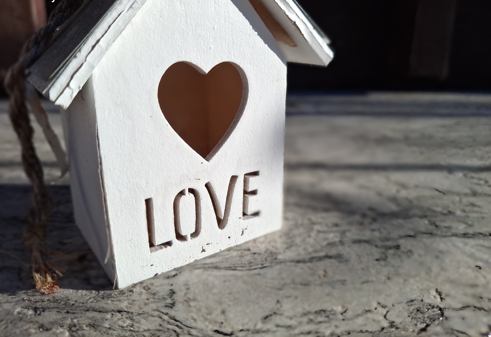 Weißes Holzhaus mit herzförmiger Öffnung und dem Schriftzug „LOVE“ im Sonnenlicht