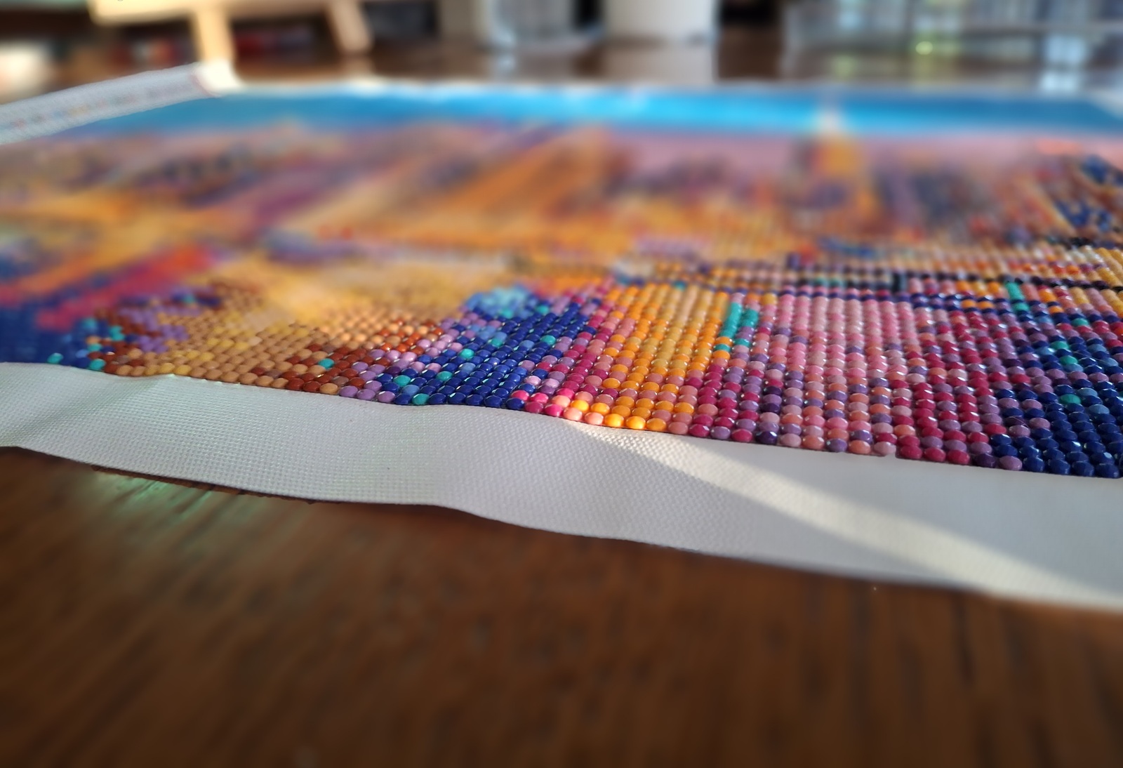 Nahaufnahme eines farbenfrohen Diamond Paintings mit vielen kleinen, glänzenden Steinchen auf einem Holztisch; der Hintergrund ist weich unscharf.