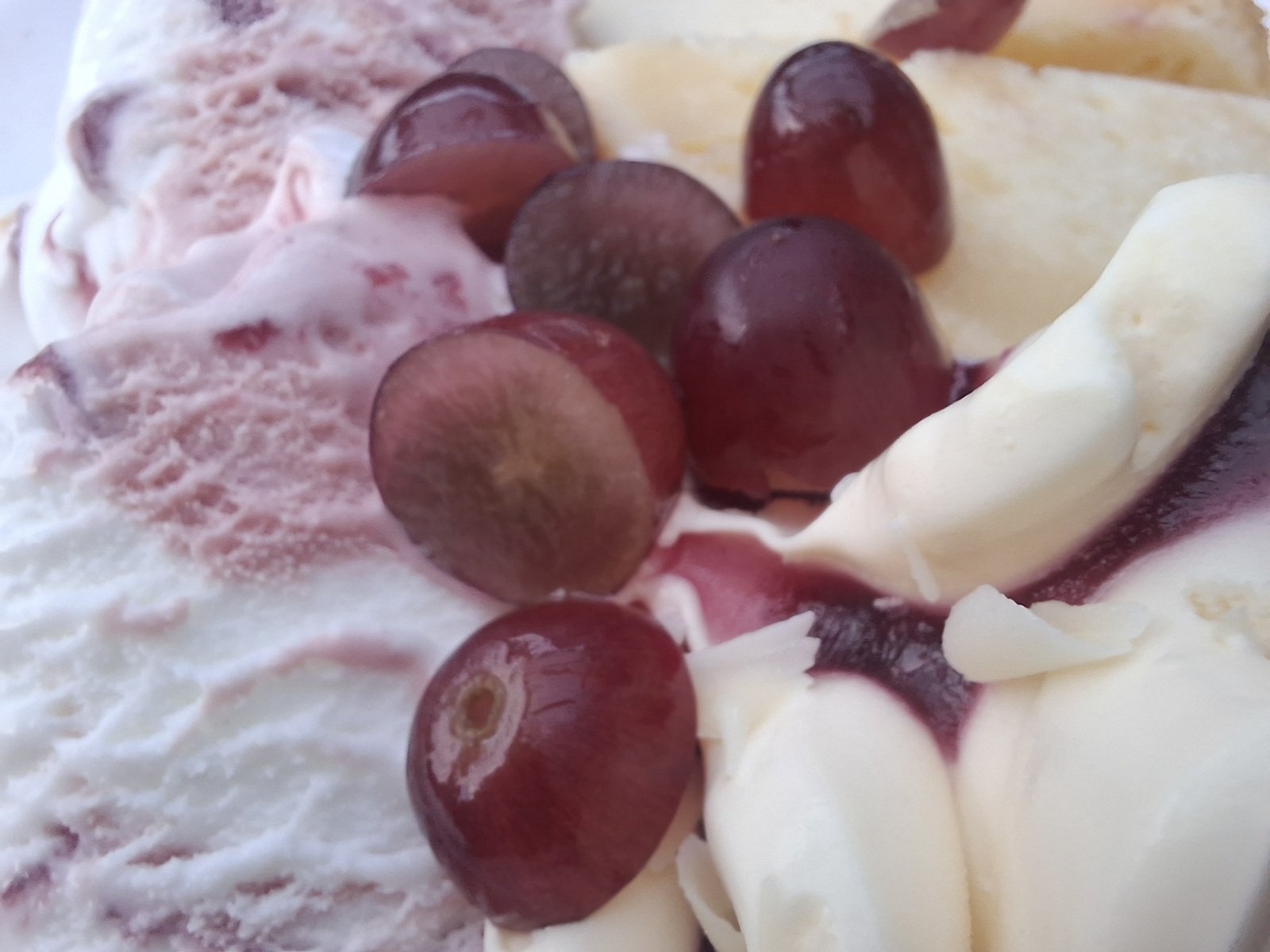 Nahaufnahme einer Mahlzeit mit roten Trauben, Obst und cremigen Bestandteilen von Speiseeis