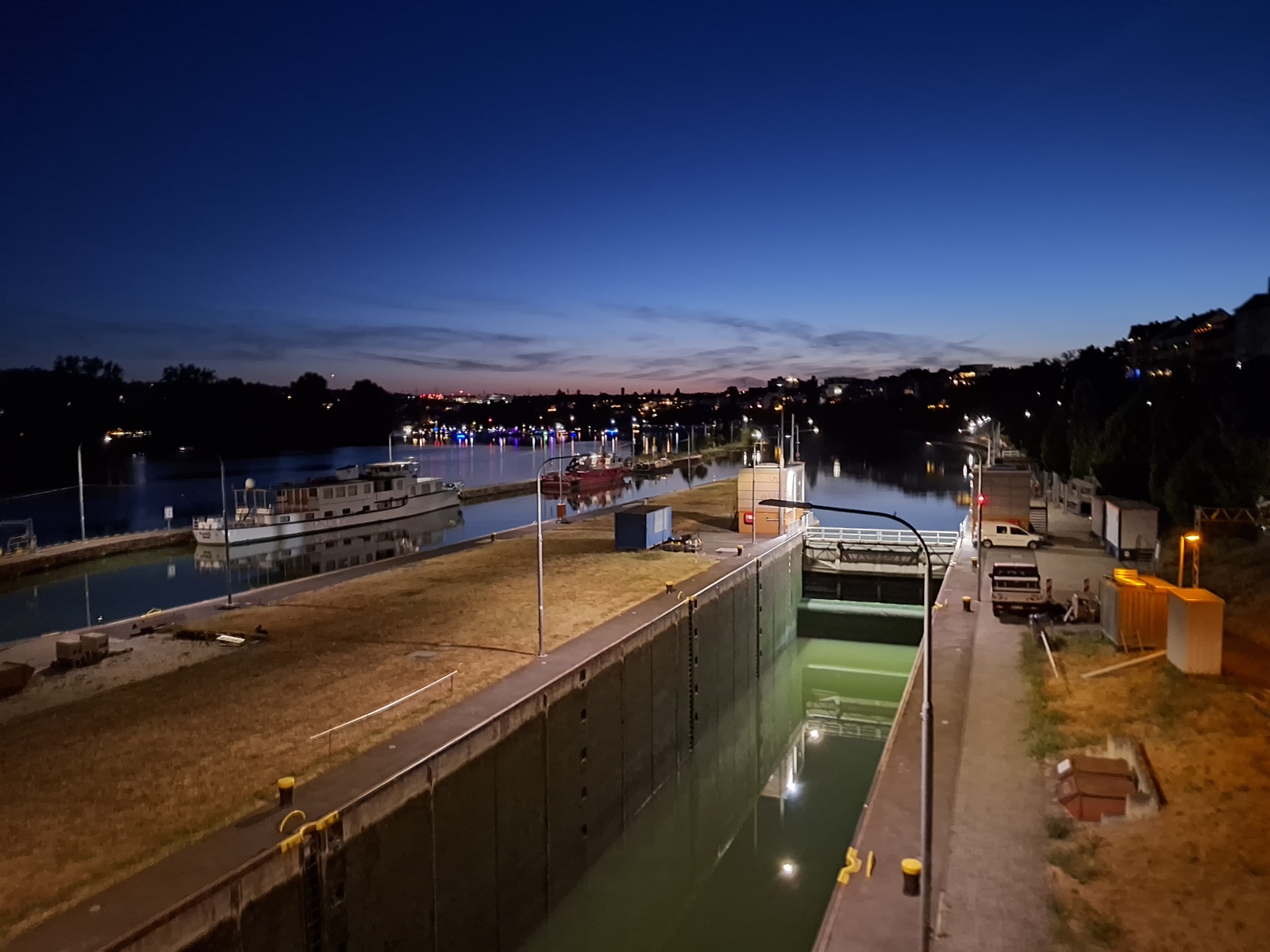 Blick von oben auf die beleuchtete Schleuse an der Mosel in Koblenz während der Abenddämmerung.